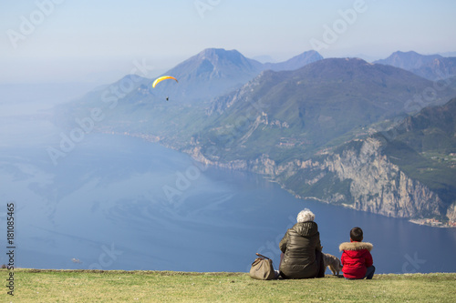 Madam and child look at the paratrooper flying over Garda lake, Baldo mount, Verona, Italy