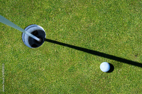 Golf green with golf ball next to the hole, with the flag pole in 