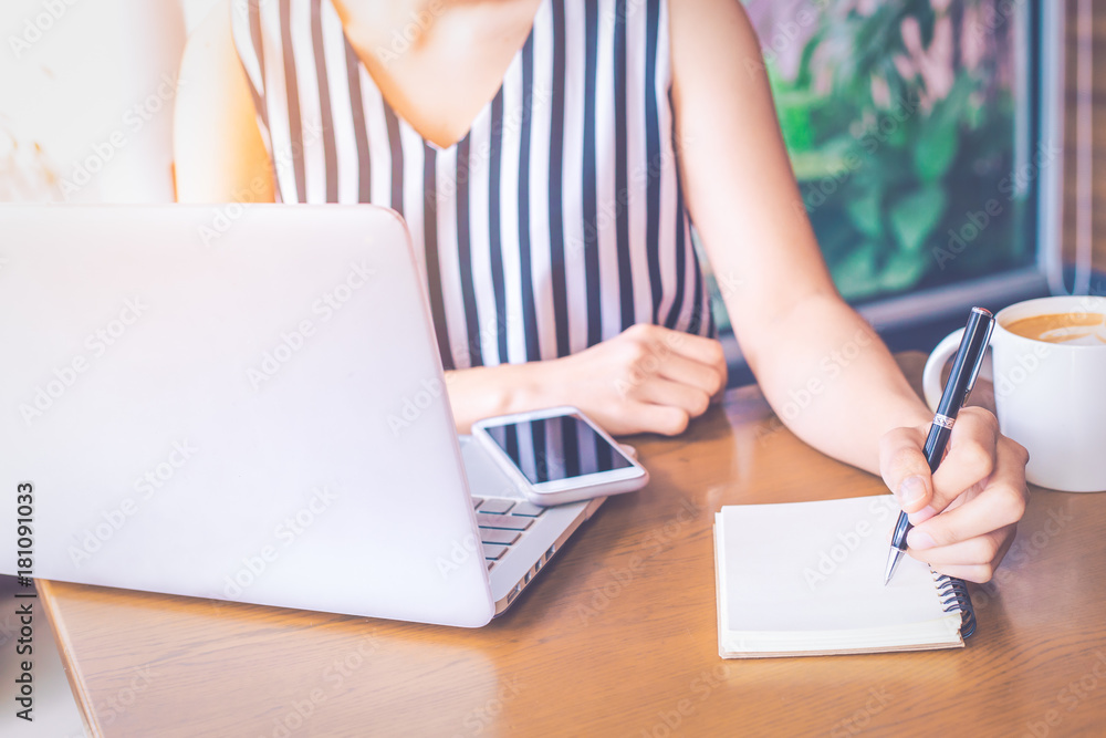 Business woman hand writing in notepad with a pen and using laptop computer in office. Business woman hand writing in notepad with a pen and using laptop computer in office.