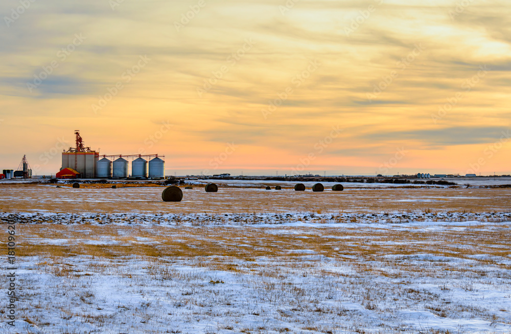 Metal barns and granaries in the snowy winter field at sunset of the day