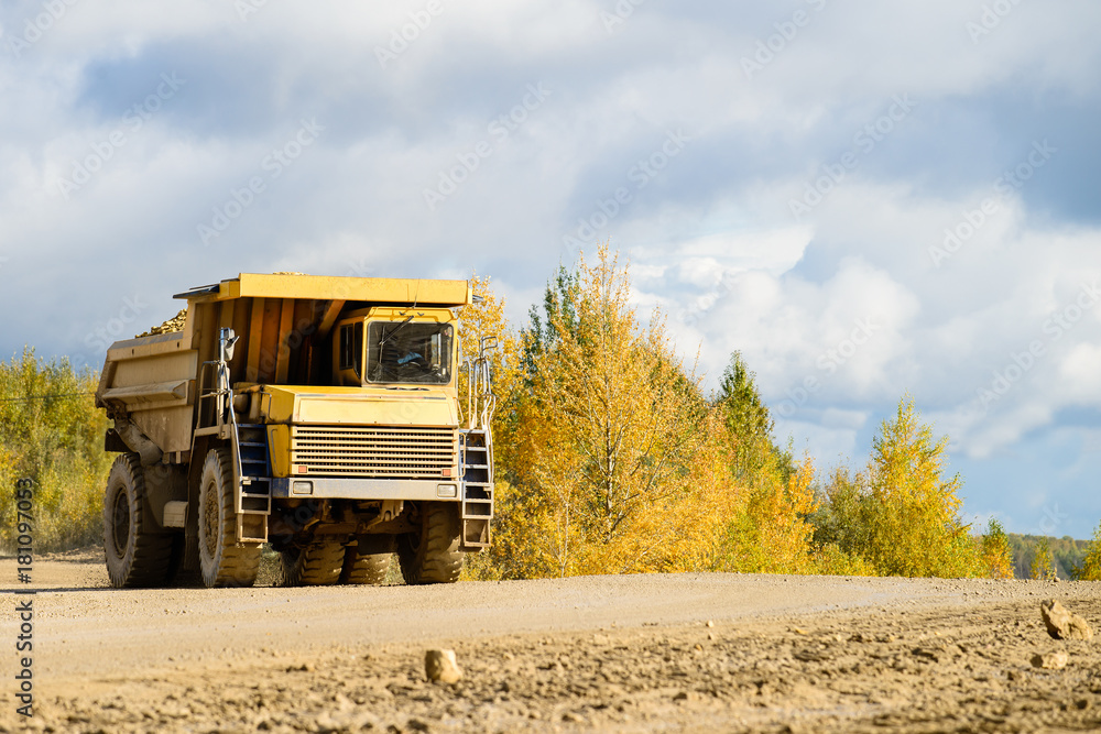 Big yellow mining truck transporting materials down a dirt road on a sunny day Big yellow mining truck transporting materials down a dirt road on a sunny day