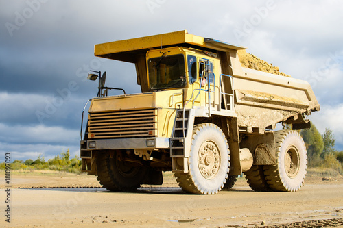 Big yellow mining truck transporting materials down a dirt road on a sunny day