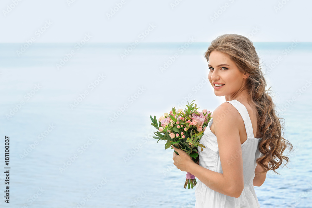 Young smiling bride in white gown holding bouquet on seashore Young smiling bride in white gown holding bouquet on seashore