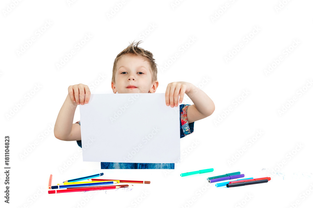 A 6 year old boy in a blue shirt paints with pencils on a white background isolate