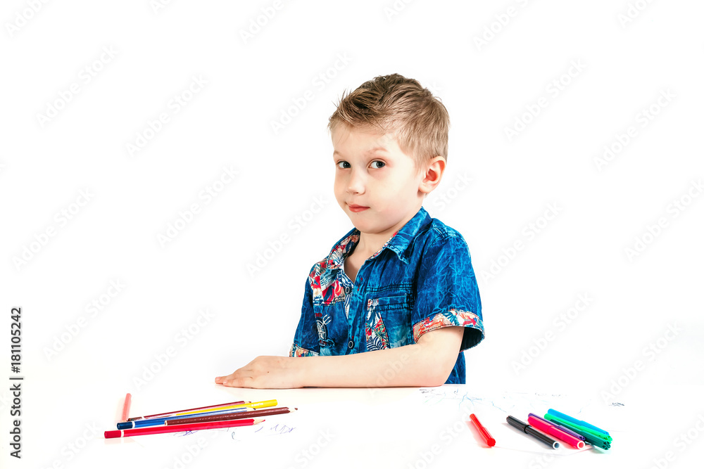 Young cute boy wearing a blue shirt with colored pencils on a white background. The concept of suspicion Young cute boy wearing a blue shirt with colored pencils on a white background. The concept of suspicion