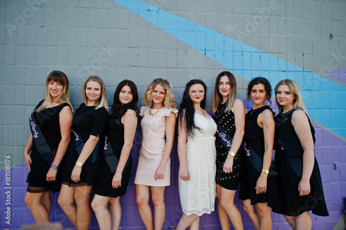 Group of 8 girls wear on black and 2 brides at hen party against colourful wall.