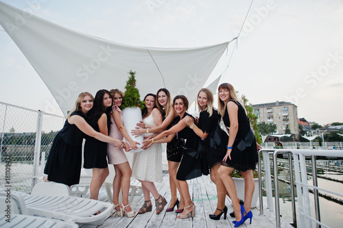 Group of 8 girls wear on black and 2 brides at hen party having fun at pier on beach side.