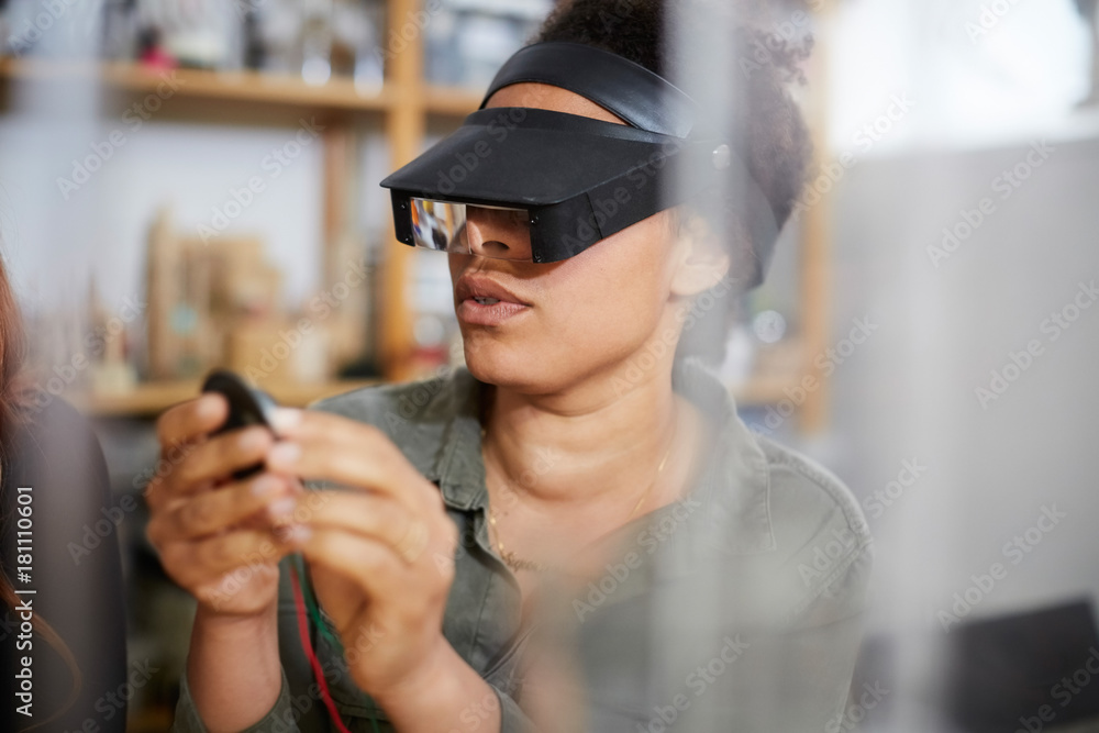 Female technician looking at electrical component through loupe in workshop Female technician looking at electrical component through loupe in workshop