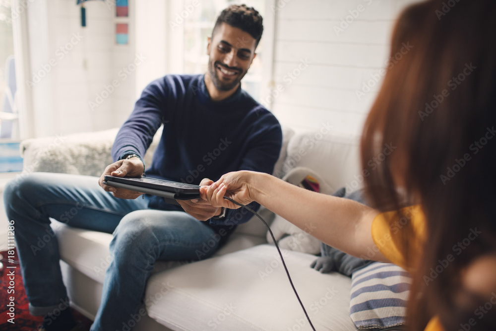 Cropped image of woman assisting man in charging digital tablet at home Cropped image of woman assisting man in charging digital tablet at home