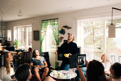 Playful young man catching snack with mouth while friends watching him in cottage