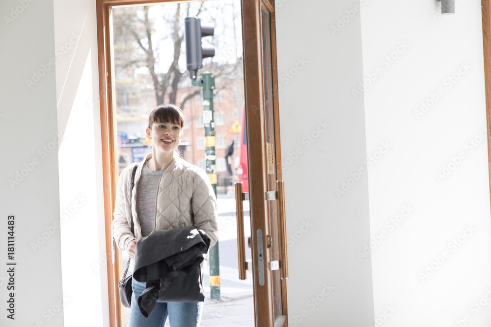 Smiling young woman standing with overcoat at doorway Smiling young woman standing with overcoat at doorway