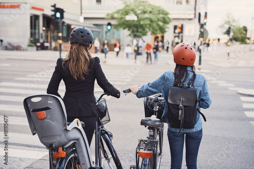 Rear view of females with bicycles crossing street in city