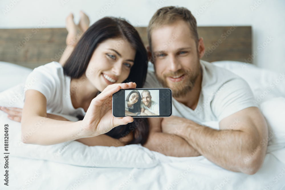 Keep smiling. Delighted couple lying on the bed and keeping smiles on faces while posing on camera