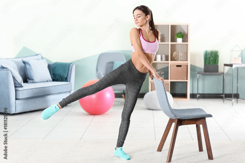 Beautiful young woman doing exercises with chair at home