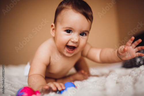 Child in a diaper stands on the bed covered with soft white blanket