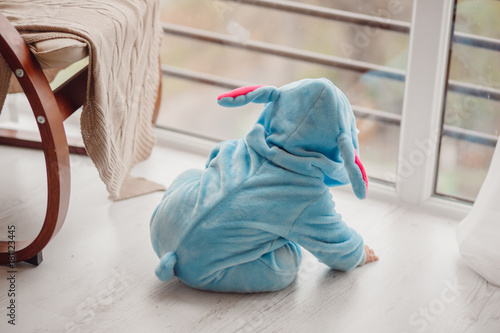 Little baby in blue suit looks like a Stitch sitting on the floor before bright window © pyrozenko13