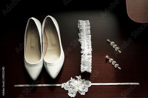 White women's wedding shoes, garter, earrings on a dark wooden background photo