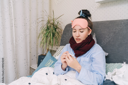 Young Sick woman with flu and tempreture in bed is looking at thermometer photo