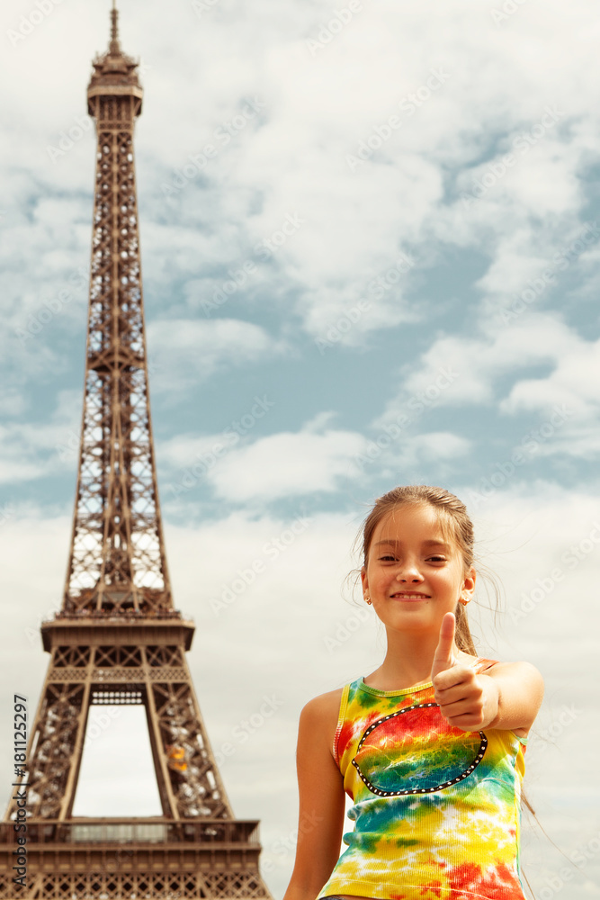 Cheerful smiling girl tourist showing thumbs up success sign in front of Eiffel Tower, Paris