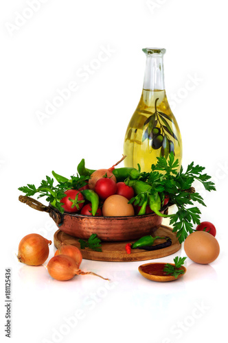 close-up still life with mixed vegetables in frypan, eggs and olive oil isolated on white background