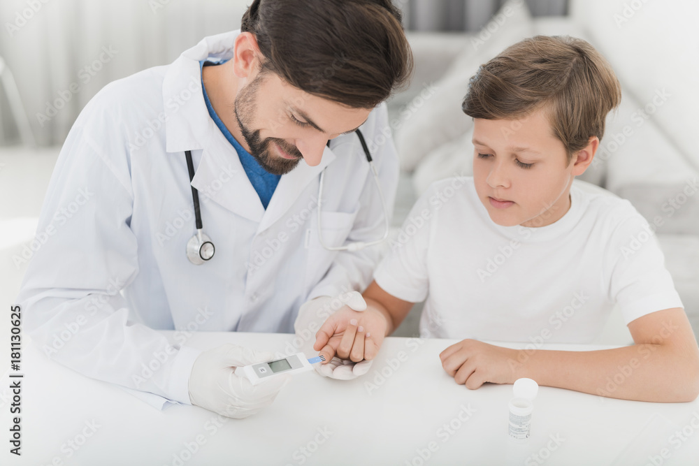 The doctor takes the blood from the boy with a finger using a scarifier. The boy staunchly endures the procedure. The doctor takes the blood from the boy with a finger using a scarifier. The boy staunchly endures the procedure.