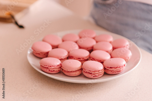 Close up pink sweet macaroons on white plate. French tasty cookies, dessert. The result of cooking, homemade food, kitchen
