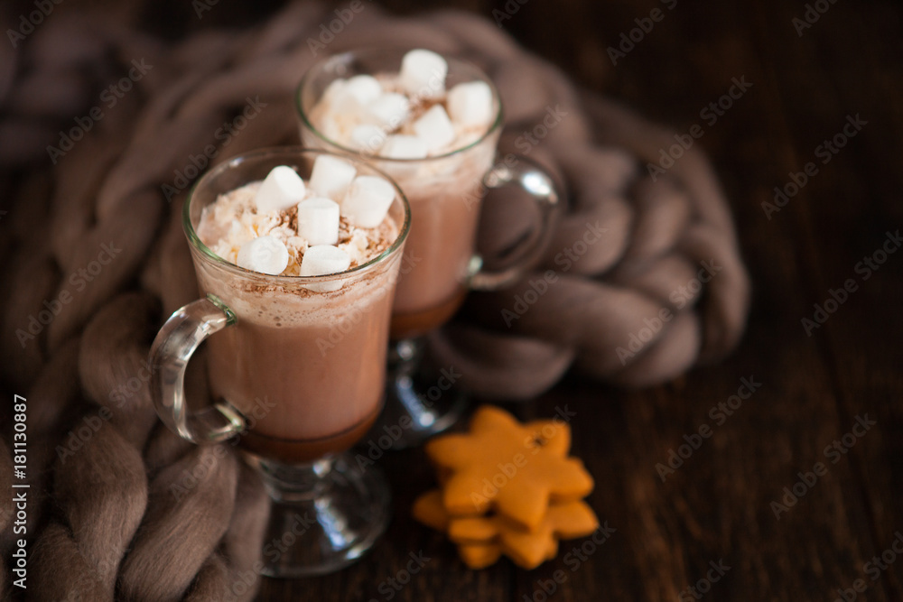 Two glasses with Hot chocolate garnished with whipped cream, marsmallow and cocoa powder on wooden background with Cozy plaid from merinose wool Two glasses with Hot chocolate garnished with whipped cream, marsmallow and cocoa powder on wooden background with Cozy plaid from merinose wool