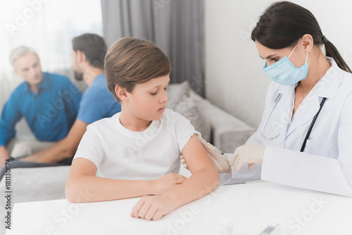 The nurse makes an insulin injection to the boy. A nurse is sitting in a mask and gloves at the table.