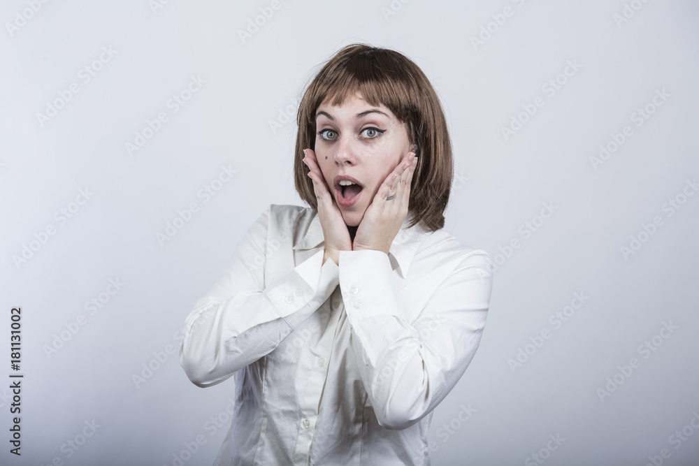 ragazza con capelli a caschetto e camicia bianca, guarda in macchina e si stupisce con le mani in faccia - sfondo grigio ragazza con capelli a caschetto e camicia bianca, guarda in macchina e si stupisce con le mani in faccia - sfondo grigio