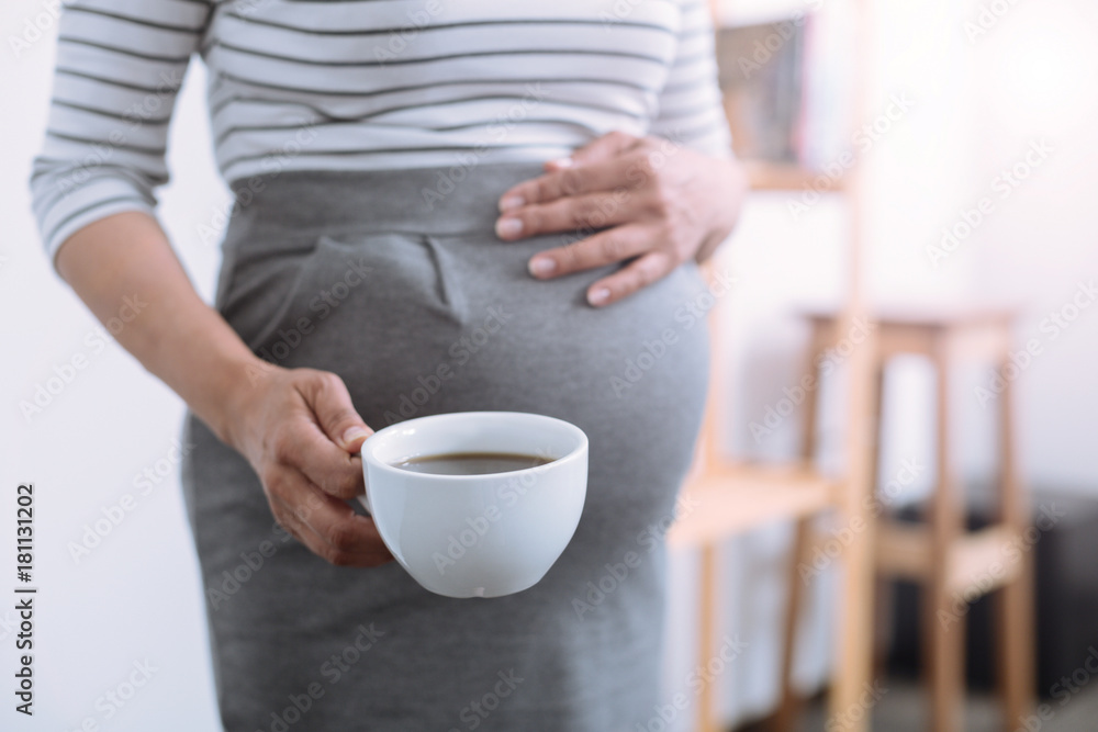 Big belly. Tender woman touching her baby abdomen and going to have break, drinking tea Big belly. Tender woman touching her baby abdomen and going to have break, drinking tea