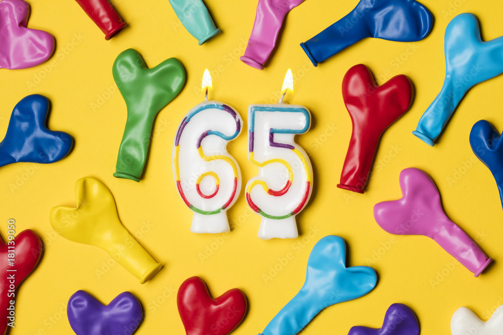 Naklejka premium Number 65 candle with party balloons on a bright yellow background