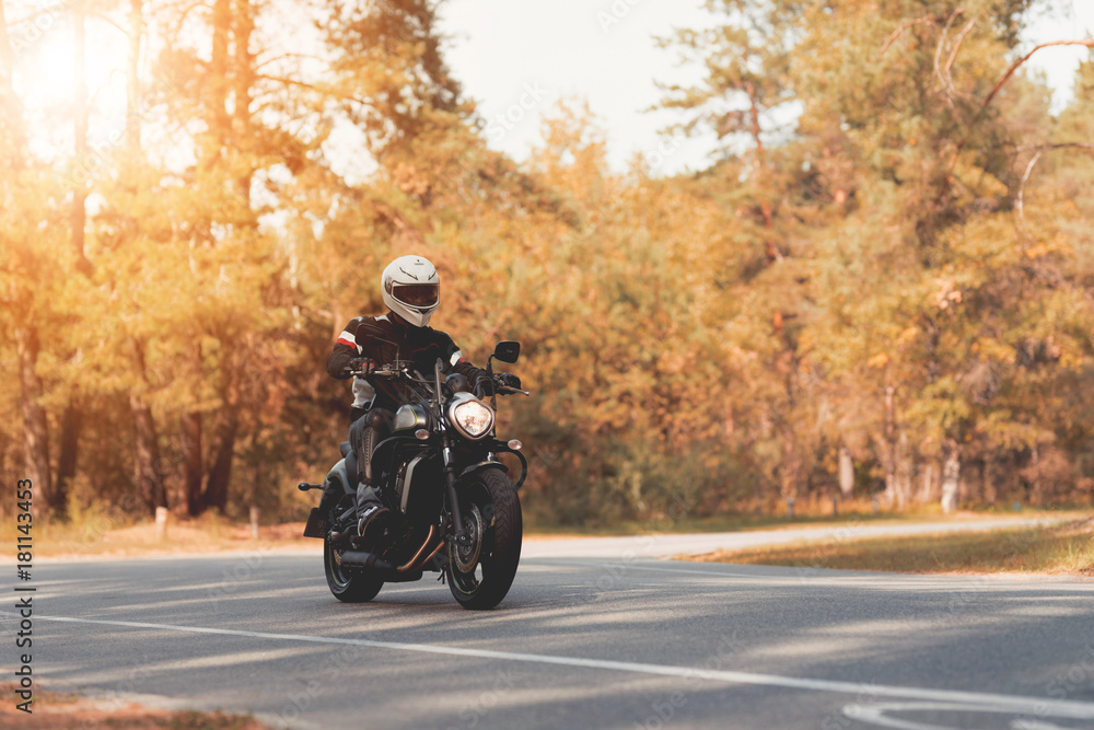 Fototapeta premium A young guy in a helmet is riding on a forest road on an electric motorcycle.