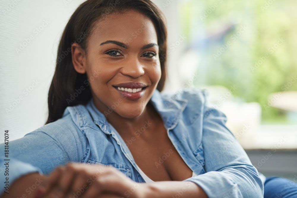Smiling young African woman sitting on her sofa at home Smiling young African woman sitting on her sofa at home