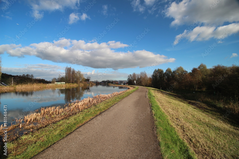 Blue sky and big clouds are reflecting in river Rotte with dike and cycle road in Oud Verlaat, Netherlands 