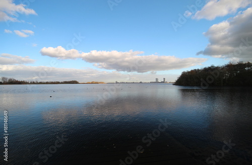 Blue sky with big cloud reflecting on water named Zevenhuizerplas in Oud Verlaat. At the horizon is a silhouette of the Nesselande district of Rotterdam visible