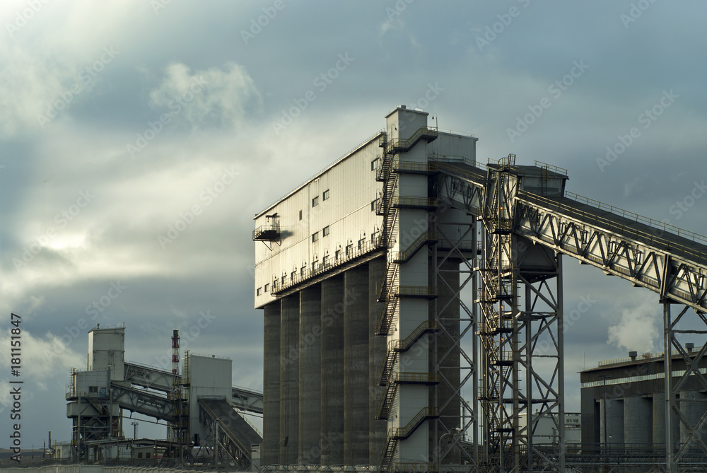 a fragment of a modern industrial enterprise with several silos for storage of loose materials and an inclined covered belt conveyors