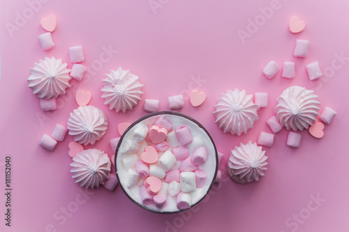 Top view hot beverage with whipped cream,marshmallows and heart shaped chocolate candies on pink pastel background