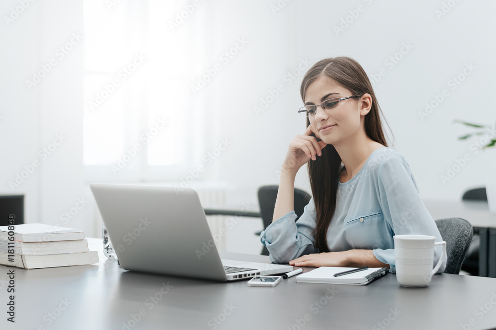 Delighted young woman looking at laptop screen in office. Delighted young woman looking at laptop screen in office.