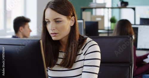 Portrait of young attractive woman working on the computer in the modern office. Office workers on the background. Close up. photo
