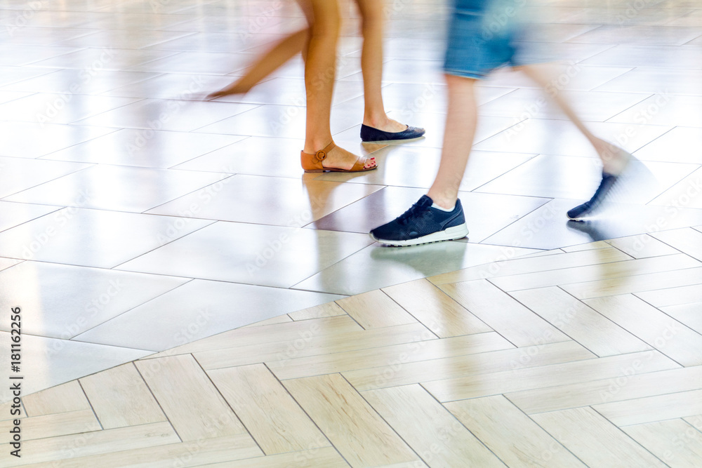 People walking on the tiled floor - Detail of legs and shoes moving on sidewalk in mall. Blur in Motion, Long Exposure. Abstract Background People walking on the tiled floor - Detail of legs and shoes moving on sidewalk in mall. Blur in Motion, Long Exposure. Abstract Background