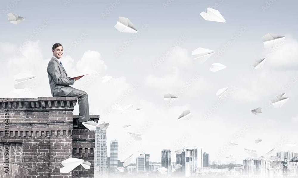 Man on roof edge reading book and cityscape at background Man on roof edge reading book and cityscape at background