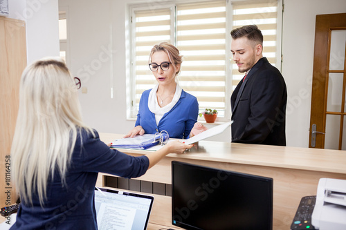 Successful Business lady in the waiting area looking at secretary and showing her some documents in a folder next to her partner