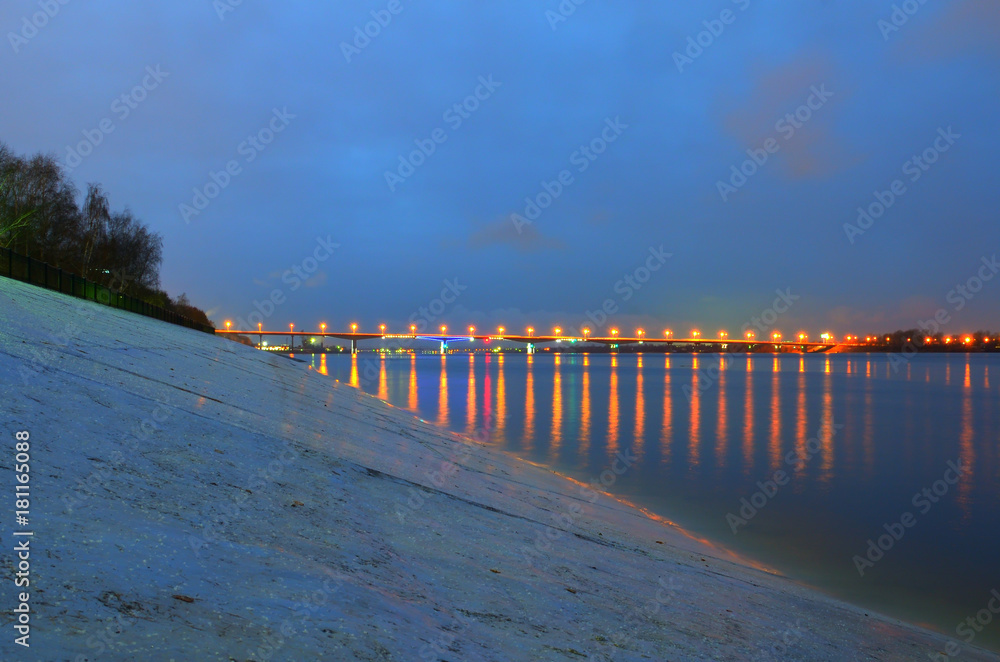 Night city embankment in Perm and bridge through the Kama river, lit by lanterns, the reflection of light in water.