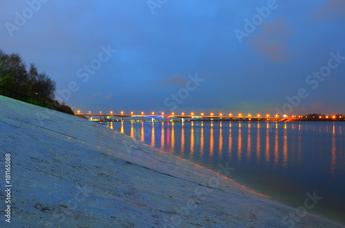 Night city embankment in Perm and bridge through the Kama river  lit by lanterns  the reflection of light in water.