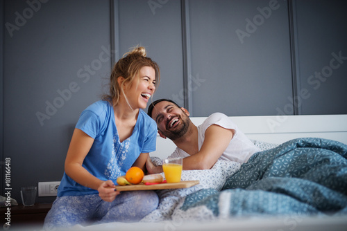 Slika na platnu Beautiful happy young romantic girl brings breakfast to her husband in the bed and laughing together after he wakes up