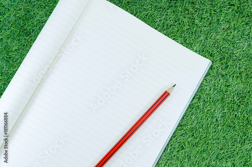 Notebook with pencil isolate on green grass background,for art education background