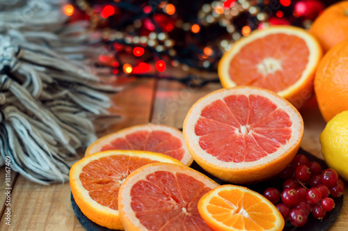 Citrus fruits on wooden table with woolen blanket and red christmas lights. Grapefruit  orange  tangerine and red currant. Christmas and new year celebration