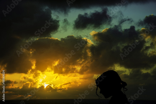 Silhouette of a young girl with sunrise over the ocean in background