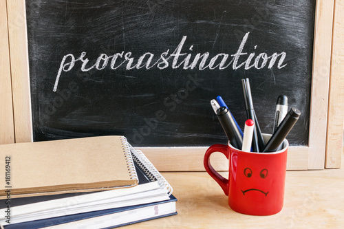 Lettering of word Procrastination on black chalkboard on a background of notepads and diary and a red cup with a sad smile. Business and pischological concept.  Self-control and achieving the goal photo