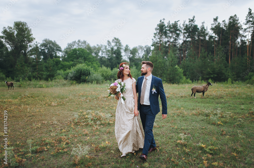 The bride and groom walk along the summer forest glade leaning against each other. The bride with a wreath of fresh flowers and with a bouquet. The bride and groom walk along the summer forest glade leaning against each other. The bride with a wreath of fresh flowers and with a bouquet.